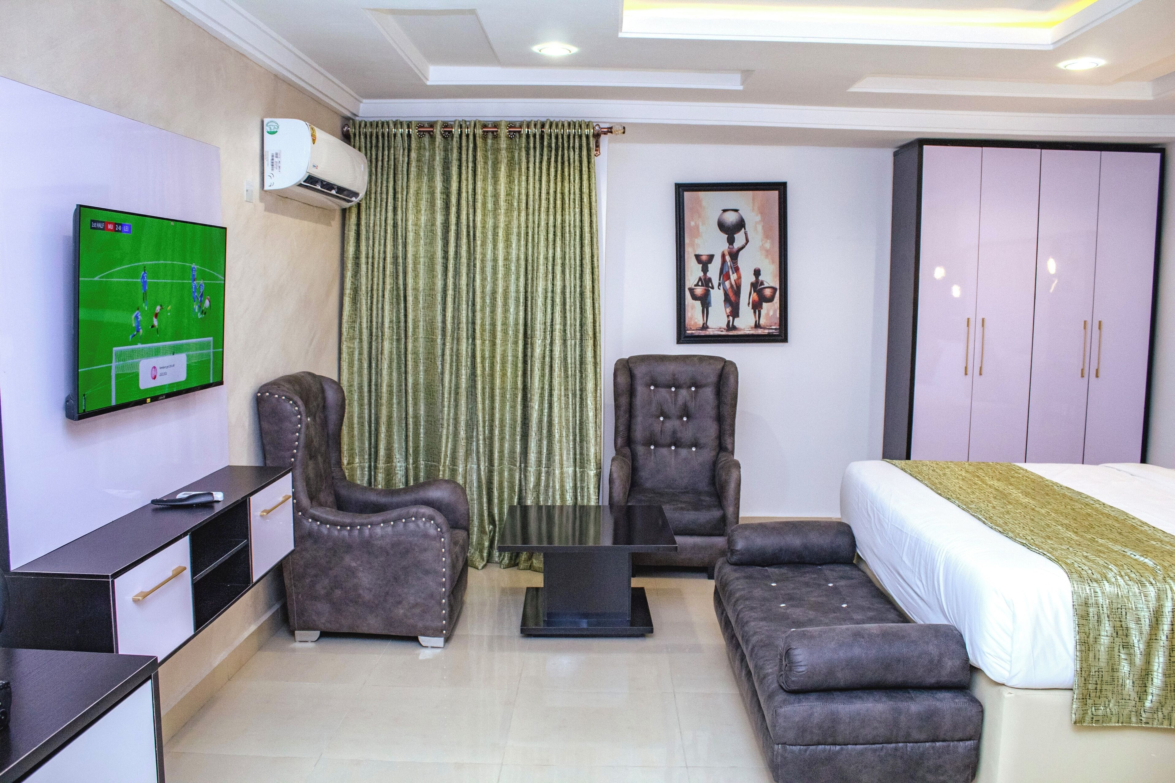 Une chambre d’hôtel équipée d’un téléviseur mural, d’un canapé, d’un fauteuil, d’un lit et d’une armoire.