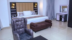Ein Hotelzimmer mit einem Bett, einem Sessel, einer Couch, einem kleinen Tisch, einem Spiegel und einem Fenster mit Vorhängen.