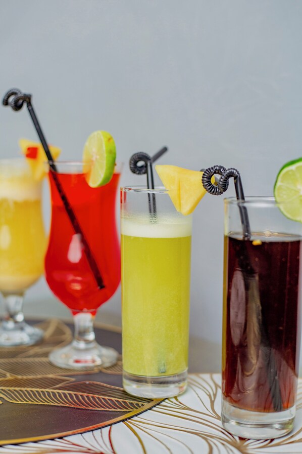 Three cocktails with straws and lime garnishes on a table with a patterned tablecloth.