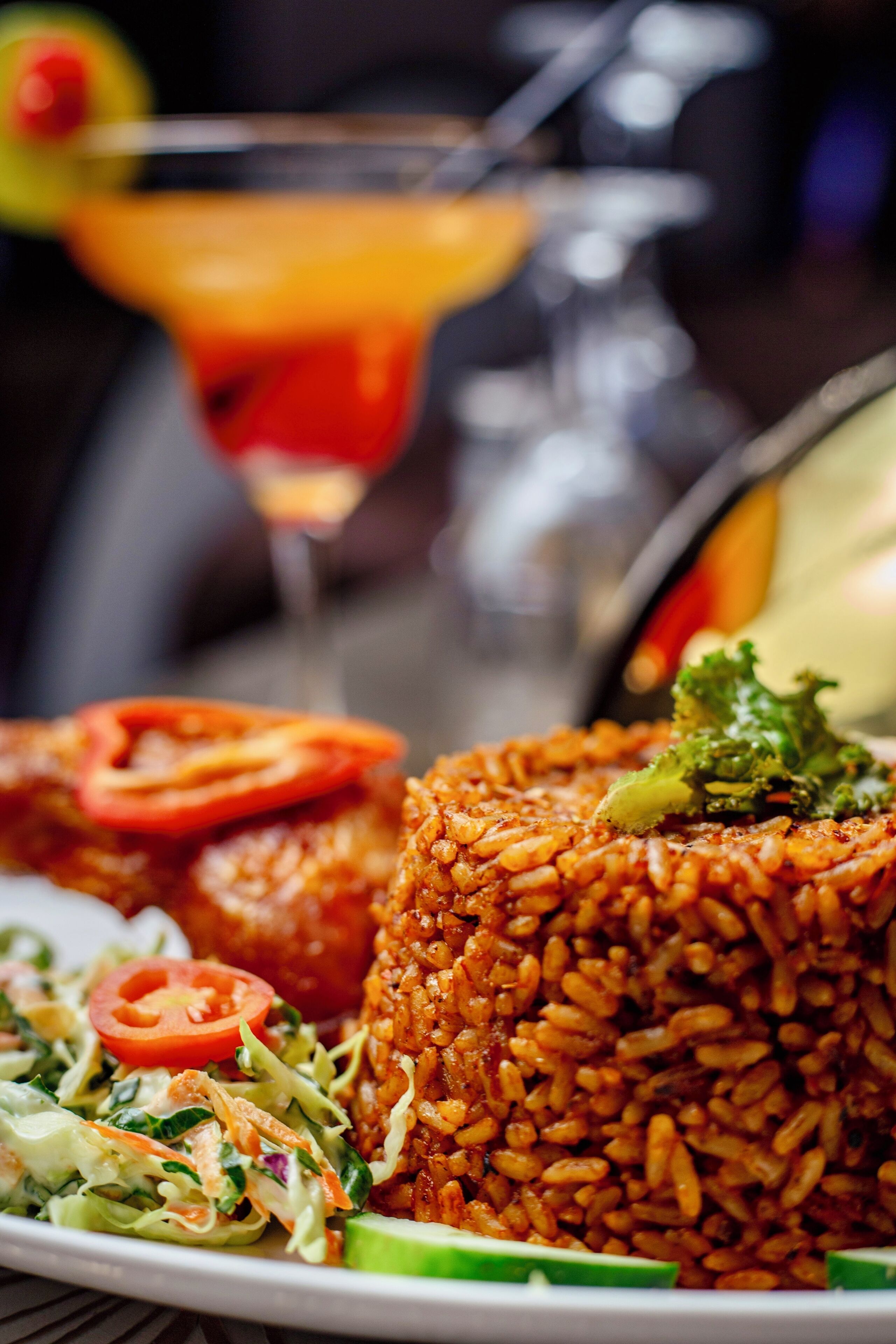Un plato de comida con arroz, verduras y un cóctel al fondo.