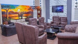 Ein modernes Wohnzimmer mit weichen braunen Sofas, einem großen Gemälde von einem Sonnenuntergang, einer Uhr und einem flachbildschirmfernseher an der Wand.