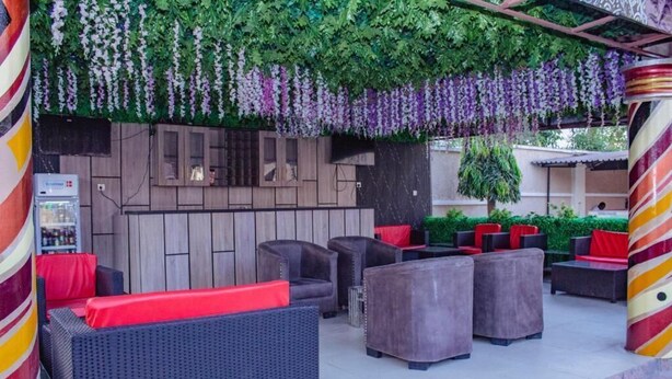 Ein Außenbereich mit Korbmöbeln, roten Kissen, einer Holzwand mit Schränken und hängenden violetten Blumen.