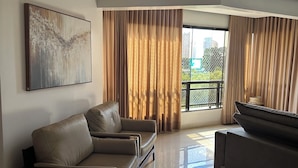 A modern living room with a sofa, a coffee table, and a large window with curtains. - Make yourself at home (Goiania)