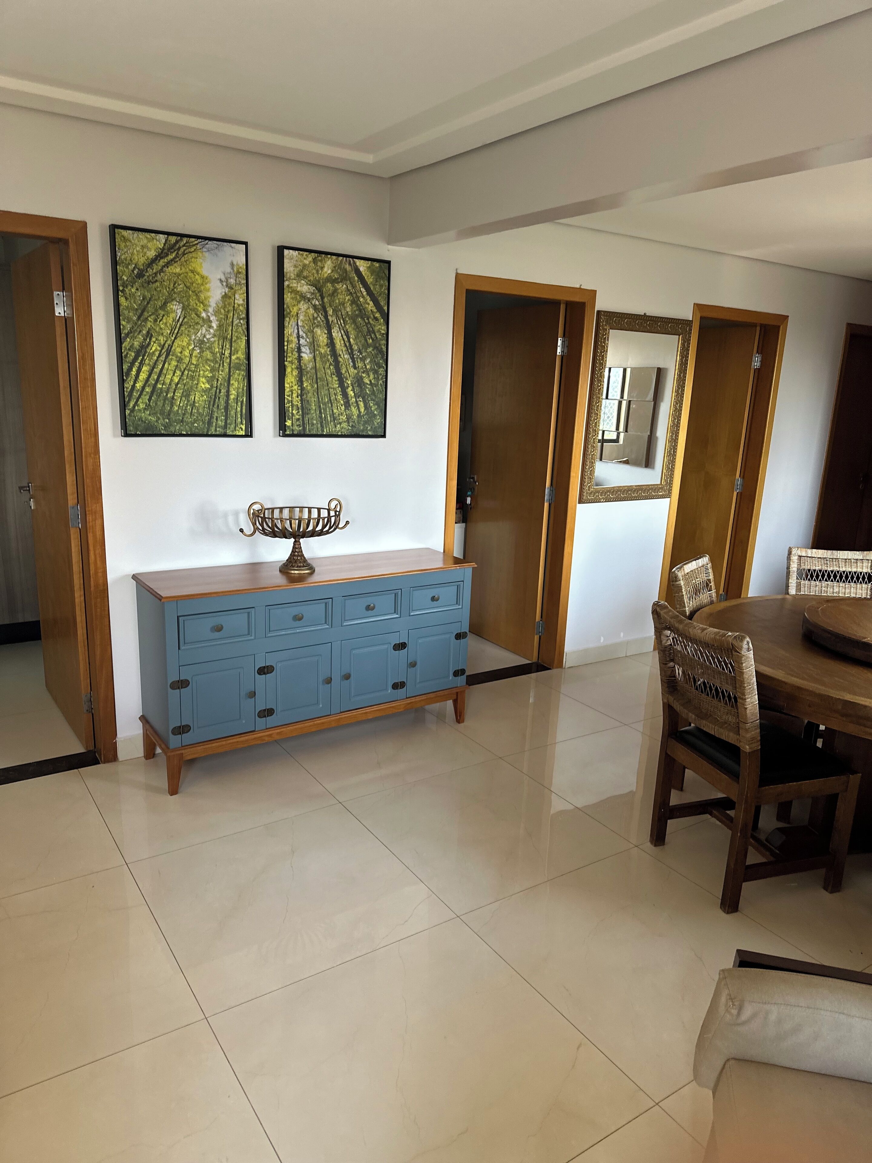 A dining area with a wooden table and chairs, a blue cabinet with drawers, and two framed pictures on the wall.