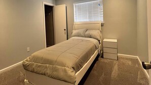 A bedroom with a bed, a nightstand, a window with blinds, and a door.