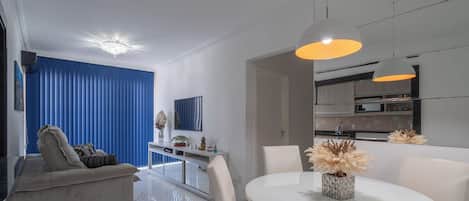 A modern living room with a sofa, a dining table with chairs, a TV, and decorative plants.