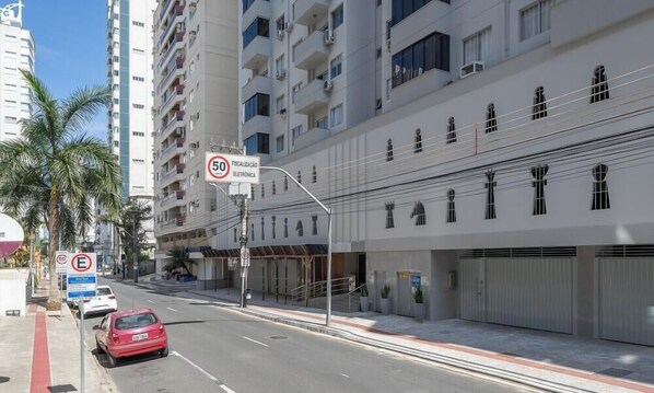 Una veduta di strada con un'auto rossa parcheggiata sul lato, un attraversamento pedonale e un edificio con diversi piani e balconi.