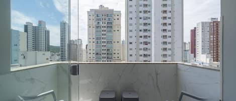 A balcony with a city view, two small stools, and a chair.