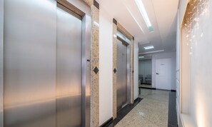A hallway with a polished floor, a service elevator, and a door with a sign. -  Apto Charmoso no Coração de BC EMF1003 (Balneário Camboriú)