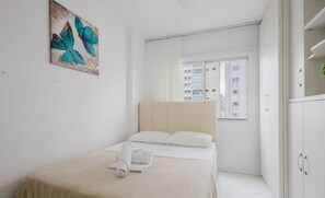 A modern bedroom with a bed, a painting, and a view of buildings. -  Apto Charmoso no Coração de BC EMF1003 (Balneário Camboriú)