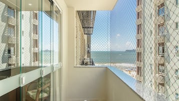 A balcony with a glass door, a wicker chair, and a view of a building and the sea.