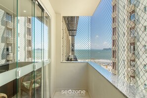 Un balcon avec une porte vitrée, une chaise en osier et une vue sur un immeuble et la mer.