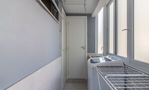 Un couloir étroit avec une porte blanche, une fenêtre munie d’une grille en métal et une petite fenêtre donnant sur l’extérieur.