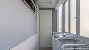 Un corridoio stretto con una porta bianca, una finestra con un portariviste in metallo e una piccola finestra con vista all'esterno.