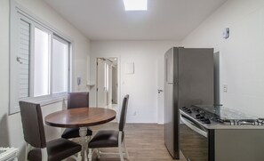 A compact kitchen with a refrigerator, stove, and dining area with chairs and a table. - 3BR Apt w/ sea View in BC Downtown Eoa0803 (Balneário Camboriú)