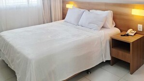 Una habitación de hotel con cama, mesita de noche, teléfono y ventana con cortinas.