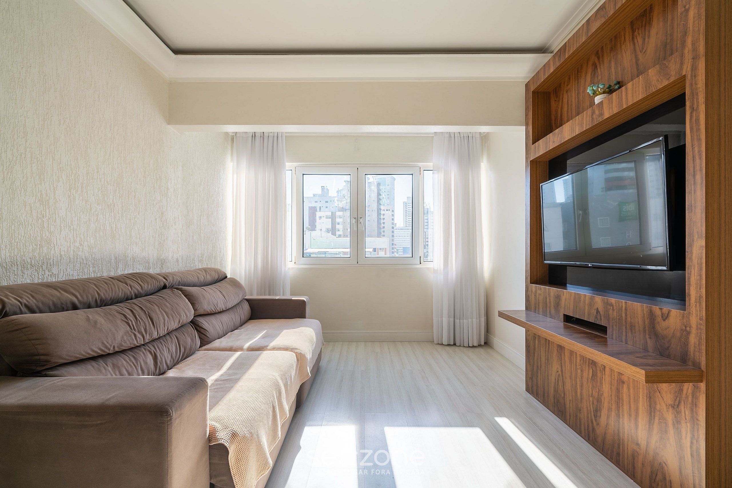 A modern living room with a sofa, a flat-screen TV, and a window with curtains.