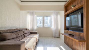 A modern living room with a sofa, a flat-screen TV, and a window with curtains.