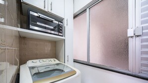 Un'area lavanderia con lavatrice e asciugatrice, una finestra con persiana decorata e uno schienale piastrellato.