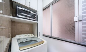 Ein Waschbereich mit Waschmaschine und Trockner, ein Fenster mit strukturierter Jalousie und einer Fliesenrückwand.