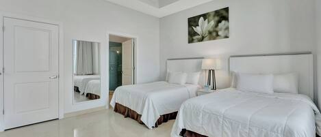 Una habitación de hotel con dos camas, un espejo grande, un cuadro y una puerta que da a un baño.