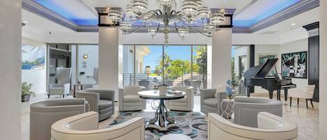 A spacious living room with a chandelier, a piano, and modern seating.