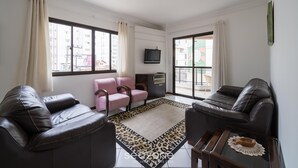 Un salon avec deux canapés en cuir, un fauteuil rose, un téléviseur et une grande fenêtre avec des rideaux.
