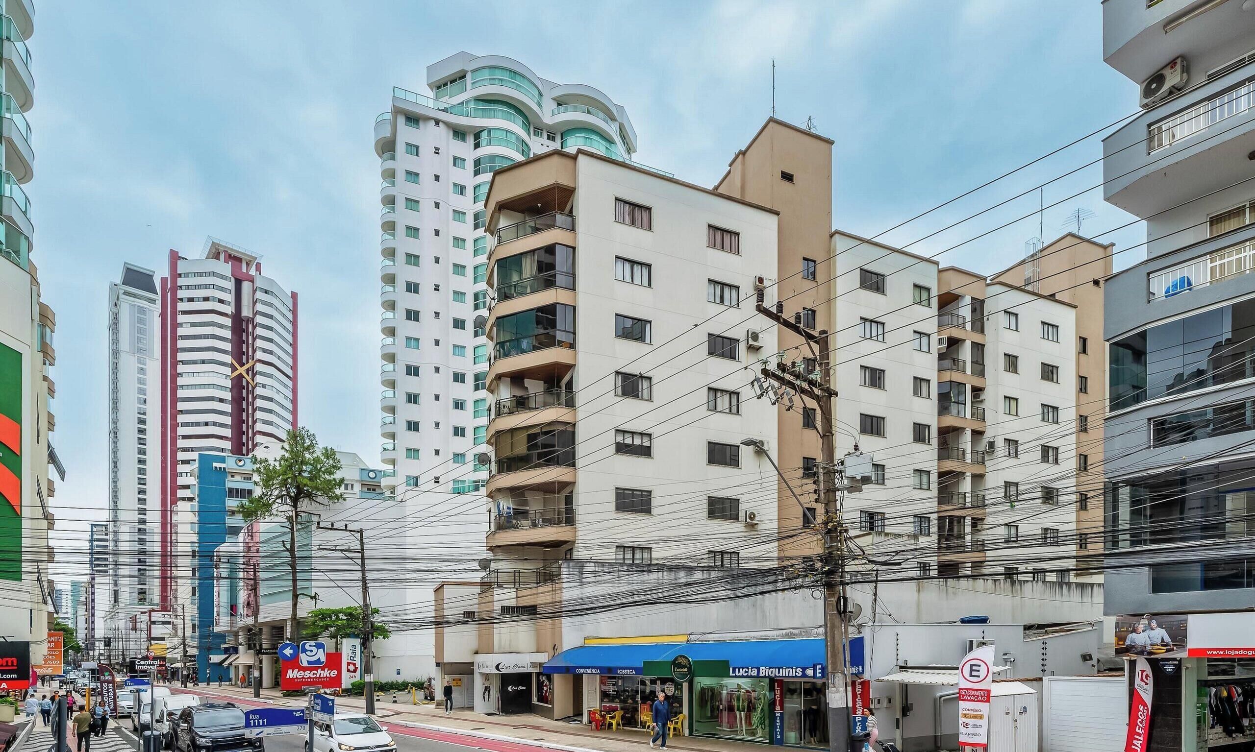 A multi-story building with balconies, a street with vehicles, and various storefronts.