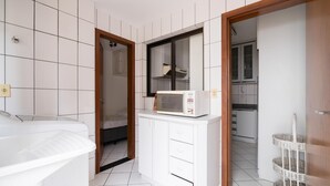 Une salle de bain moderne avec des carreaux blancs, un lavabo blanc et un four à micro-ondes posé sur un meuble blanc.