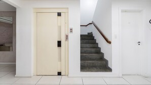 Un couloir avec une porte d’ascenseur de couleur beige, un escalier doté d’une rampe en bois et une porte blanche.