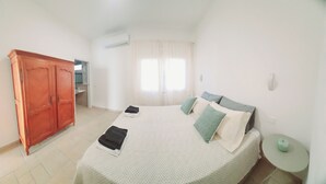 Une chambre à coucher avec un lit, une armoire, une fenêtre avec des rideaux et une petite table avec une lampe.