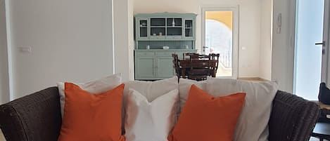 A living room with a sofa, a coffee table with magazines, and a kitchen in the background.