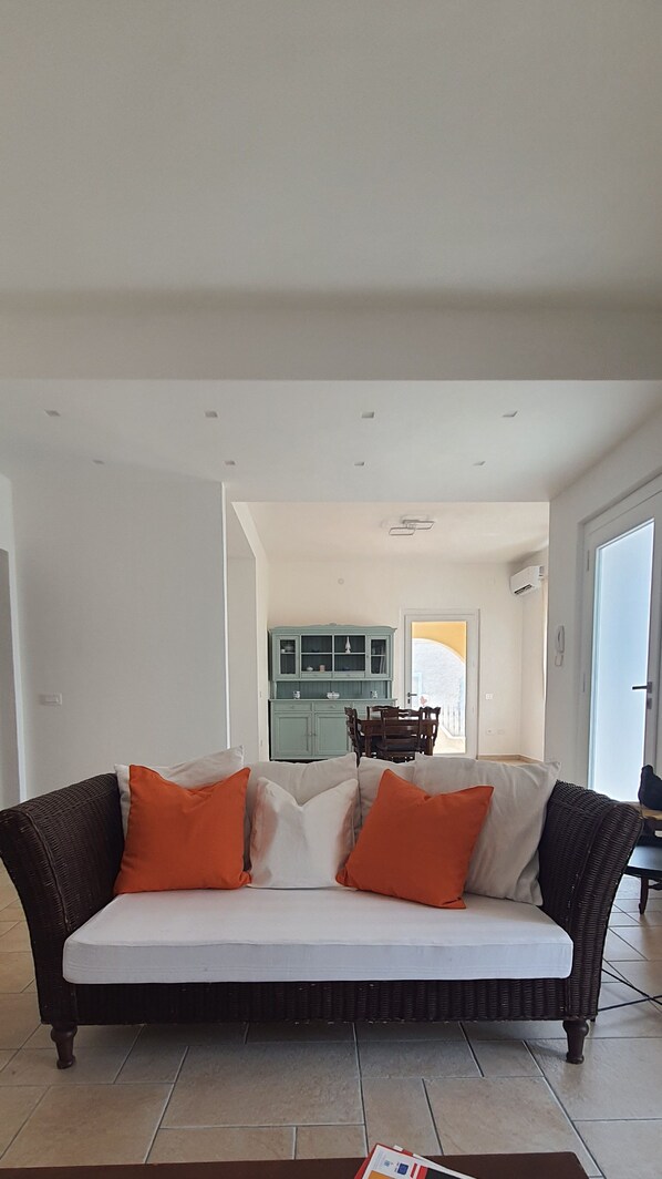 A living room with a sofa, a coffee table with magazines, and a kitchen in the background.