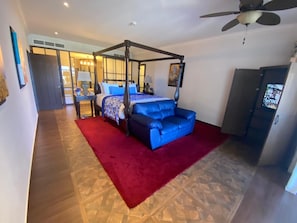 A bedroom with a four-poster bed, a blue sofa, a red rug, and a ceiling fan. - Charming 3-bedroom villa with AC, all inclusive resort in Cabo San Lucas. (El Paraje)