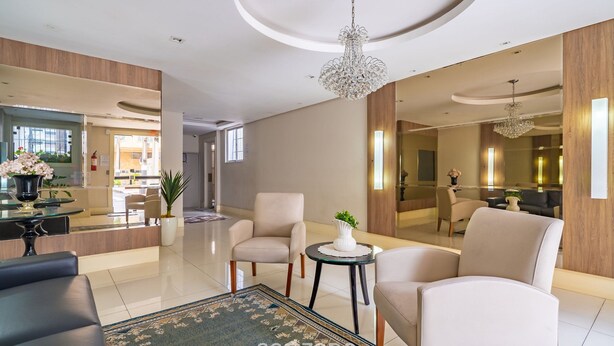A modern hotel lobby with a reception desk, seating area, and a large mirror reflecting the space. - Apartment in BC Center With Side sea View Erz0502 (Balneário Camboriú)
