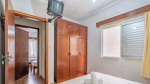 A bedroom with a wooden wardrobe, a bed with a rolled-up towel, a television mounted on the wall, and a window with blinds. - Apartment in BC Center With Side sea View Erz0502 (Balneário Camboriú)