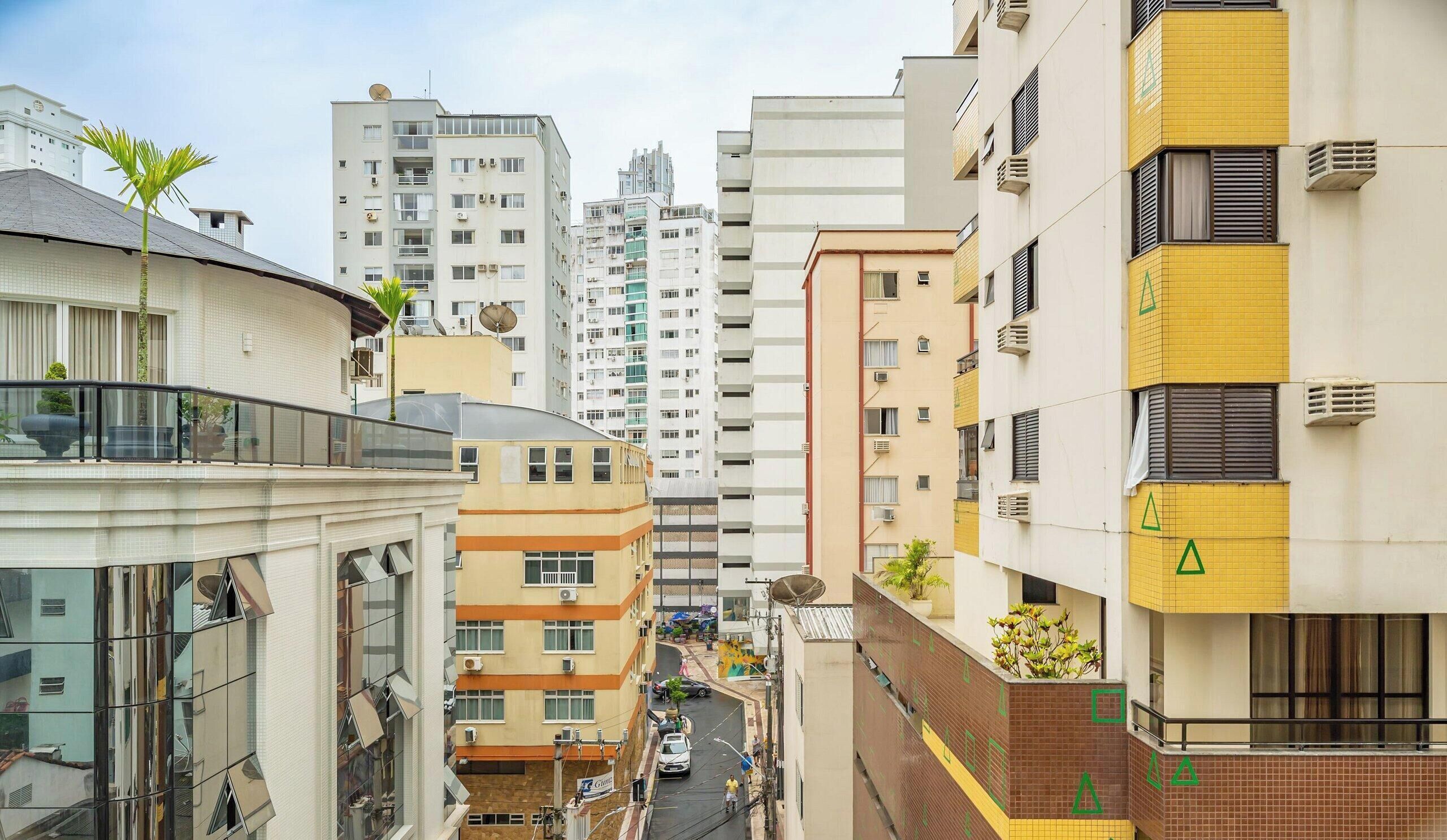 Un edificio urbano de varios pisos con balcones, vista a la calle y cielo despejado.