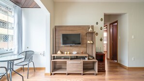 A modern living room with a wooden entertainment unit, a flat-screen TV, and a dining area with a glass table and metal chairs. - Apartment in BC Center With Side sea View Erz0502 (Balneário Camboriú)