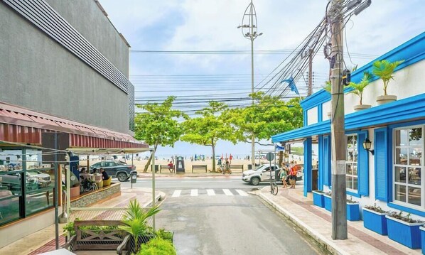 A street view with a café, a blue building with windows, and a pedestrian crossing. - Apartment in BC Center With Side sea View Erz0502 (Balneário Camboriú)