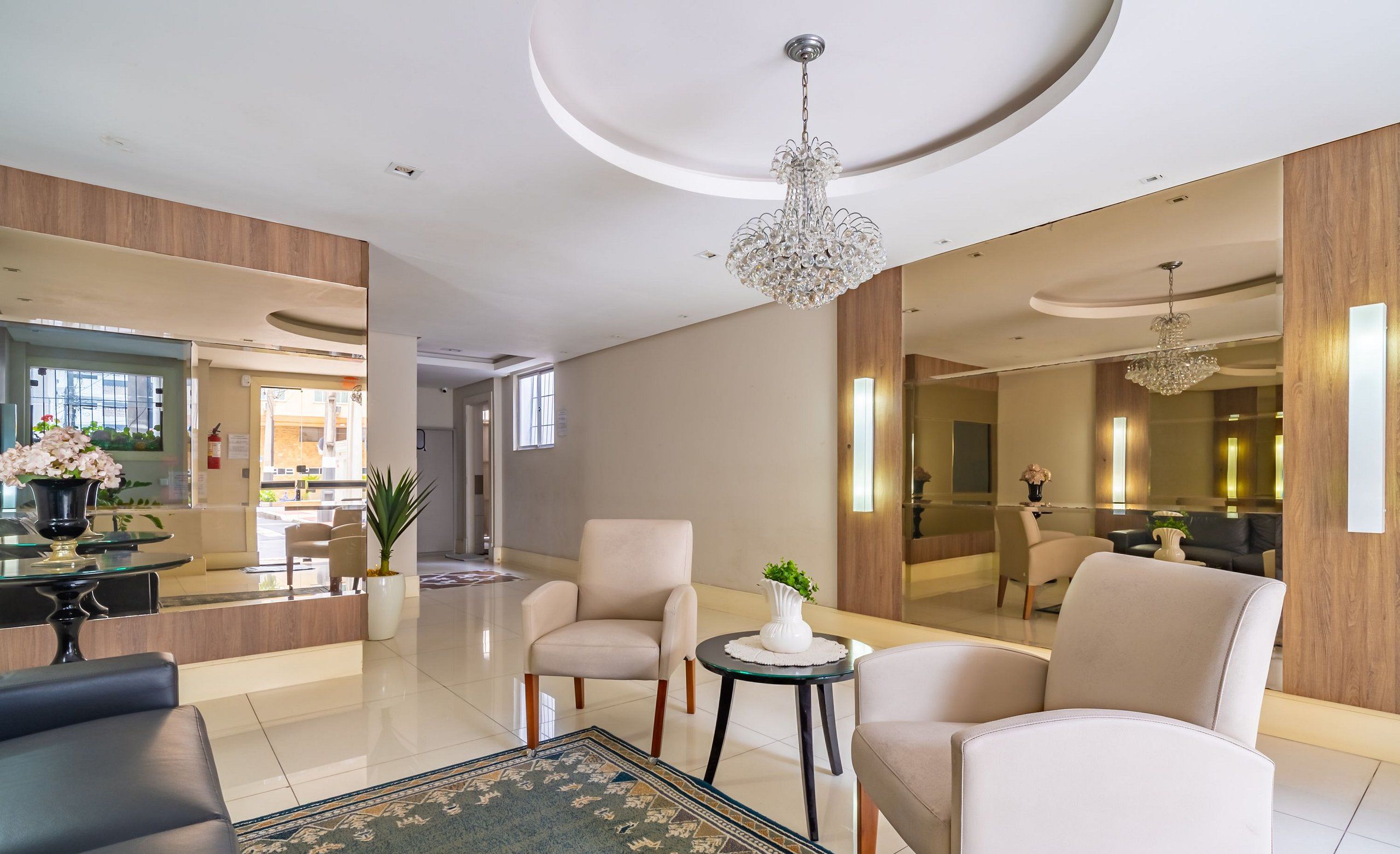 Um lobby de hotel moderno com balcão de recepção, área de estar e um espelho grande que reflete o espaço.