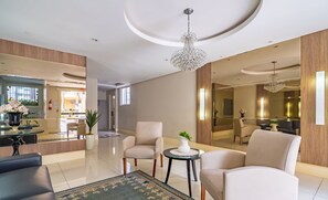 A modern hotel lobby with a reception desk, seating area, and a large mirror reflecting the space. - Apartment in BC Center With Side sea View Erz0502 (Balneário Camboriú)