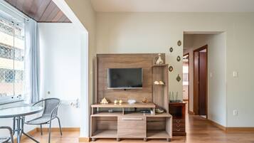Una sala moderna con un mueble de madera para entretenimiento, un televisor de pantalla plana y una zona de comedor con una mesa de vidrio y sillas de metal.