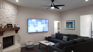A living room with a fireplace, a large abstract painting, a ceiling fan, and a couch with patterned cushions.