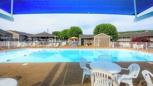 A swimming pool with lounge chairs and tables, surrounded by a fence and buildings.
