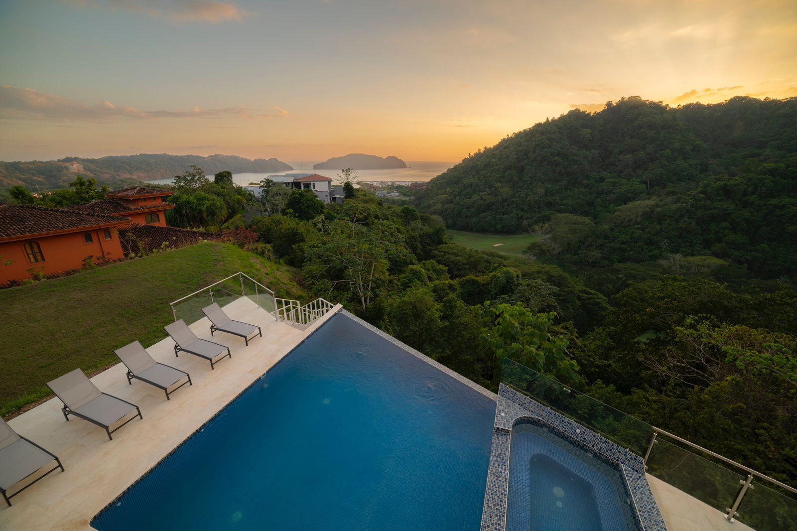 Piscina con sillas de descanso y vista a un paisaje exuberante con colinas y una extensión de agua.
