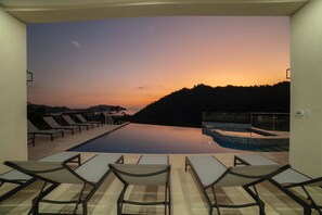 Ein Poolbereich mit Liegestühlen und Blick auf einen Sonnenuntergang über einer hügeligen Landschaft.