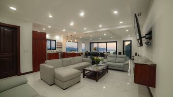 A spacious living area with a large sofa, a coffee table, and a dining area with a view.