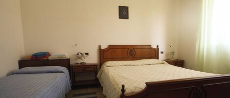 A bedroom with two single beds, a wooden headboard, a nightstand with a lamp, and a small table with a lamp.