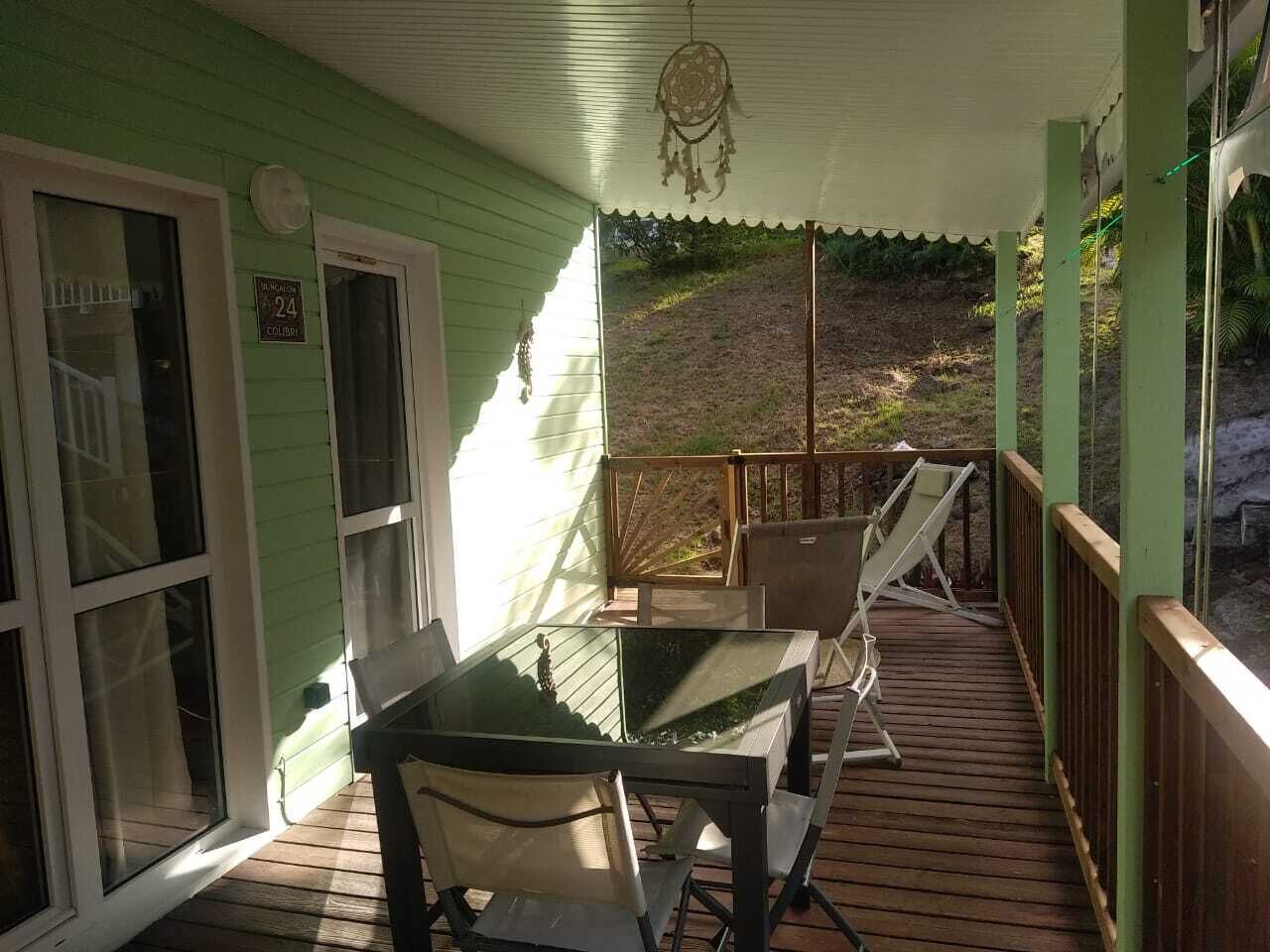 A covered porch with a table and chairs, a wooden deck, and a view of a hillside.