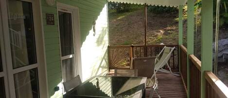 A covered porch with a table and chairs, a wooden deck, and a view of a hillside.